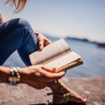 Woman sitting near the shore reading a book