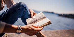 Woman sitting near the shore reading a book