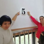 Zhan Ge and Helen pointing to a number five written on a wall.