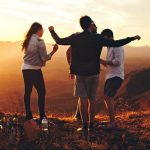 group of three to four people standing on hill at dusk, appear to be dancing