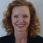 a close up a smiling white women with shoulder length red curly hair, wearing a black shirt