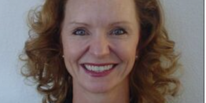 a close up a smiling white women with shoulder length red curly hair, wearing a black shirt
