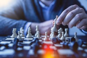 A hand picking up a chess piece with several other pieces on the chessboard.