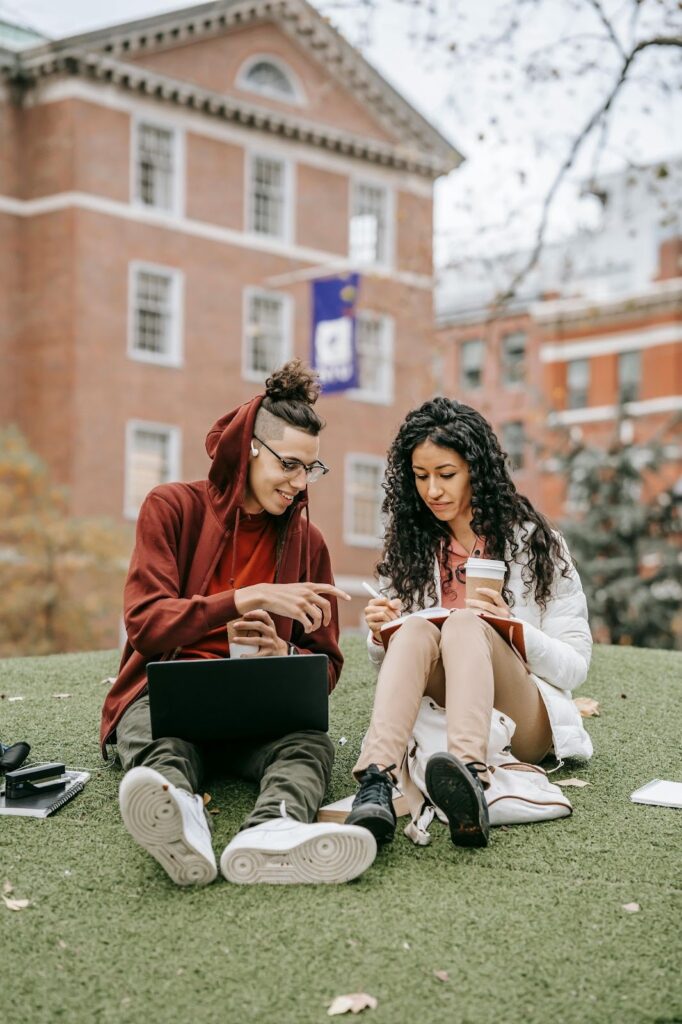 Two students sitting on grass reviewing work
